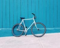white road bike leaning on teal wooden wall during daytime